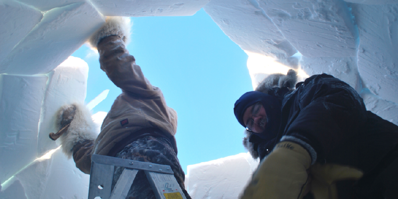 Two men inserting the final blocks of snow into the roof of an iglu