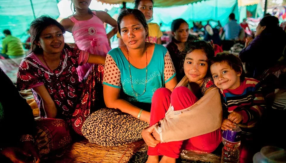 A group of women and children in a makeshift tent, looking into the camera - Humanitarian Coalition