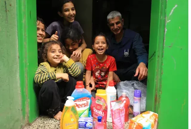A family sitting infront of a collection on household items on the floor, smiling - humanitarian Coalition