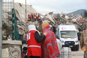 Red Crescent volunteer giving a blanket to a syria-turkey earthquake survivor and guiding them an area where they can get living essentials